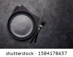 Empty plate, fork and knife. Black kitchen utensils set on stone table. Top view flat lay with copy space