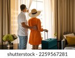 Small photo of young traveler couple with luggage looking out of the hotel room window after arrival