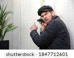 Small photo of Nosy angry obnoxious man spying on his neighbours through the window with his binoculars and mask during the coronavirus lockdown