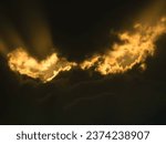 Small photo of Two bright gaps in dark clouds at sunset, like fiery eyes of a mythological monster in the sky, with sunbeams rising from both, for motifs of mystery, menace, Halloween