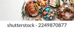 Small photo of Traditional Easter dinner or brunch with ham, colored eggs, hot cross buns, cake and vegetables. Easter meal dishes with holday decorations. Top view, copy space, panorama, banner