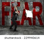 businessman holding sledgehammer hitting red FEAR word on concrete wall with large blank hole, overcoming fear concept.