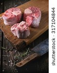 Small photo of Raw osso buco meat on wooden cutting board with vintage backsword, salt, pepper and rosemary over old wooden table. Dark rustic style
