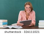 Young Happy Female Teacher With Books And Digital Tablet In Classroom