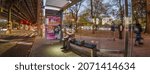 Small photo of A passenger in coats seat in a mask waiting for MTA bus on a bus stop, White Plains Road and Pelham Parkway, New York, Very wide shoot panorama, Bronx, United States of America, 11.08.2021
