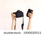 Woman holding a camera body and a lens on white wall background.