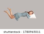 Small photo of Relaxed girl in vintage ruffle dress levitating in mid-air, sleeping on stomach lying comfortable cozy on pillow, keeping eyes closed, watching peaceful dream. indoor studio shot isolated on gray