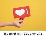 Support interesting web content, push heart button. Closeup of woman hand holding social media like icon, emoji sign to follow subscribe blog. Indoor studio shot isolated on yellow background.