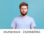 Small photo of Portrait of confident strict bearded man looking directly at camera with serious attentive face, listening attentively, unsmiling determined male. Indoor studio shot isolated on blue background.