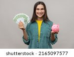 Small photo of Portrait of smiling affirmative woman holding big sum of euro banknotes and piggy bank, profitable investment, wearing casual style jacket. Indoor studio shot isolated on gray background.