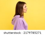 Small photo of Side view of young serious unsmiling strict woman looking at camera with calm attentive focused expression, wearing purple hoodie. Indoor studio shot isolated on yellow background.