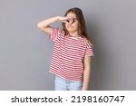 Small photo of Portrait of confused little girl wearing striped T-shirt pinching her nose to hold breath, feeling repulsion and disgust to unpleasant odor. Indoor studio shot isolated on gray background.