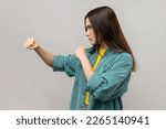Small photo of Side view of angry woman standing with clenched fists and furious look, ready to punch, expressing aggression, wearing casual style jacket. Indoor studio shot isolated on gray background.
