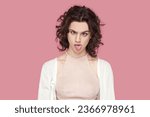 Small photo of Portrait of crazy fool woman with curly hair wearing casual style outfit having foolish facial expression, grimacing, showing bad manners. Indoor studio shot isolated on pink background.