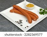 Frankfurter sausages on a plate garnished with mustard and parsley.