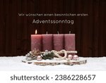 First Advent: Advent decoration with pink candles and Christmas decorations in the snow. German inscription says we wish you a peaceful first Sunday in Advent.
