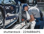 Small photo of Professional Driver Securing Brand New Car for Delivery on Flatbed Tow Truck Using Tie Down Straps. Transportation Industry Theme.