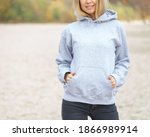 The front view of unrecognizable woman wearing light grey hoodie. She stands on the beach. Copy space on empty area on her blouse for design or inscription. Fashion mockup. Sweatshirt template.