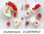 camembert and goat cheese decorated with slices of fig fruits, red currants and rosemary, on white wooden background, top view