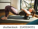 Young woman using a foam roller while doing stretching exercises at home in morning sunshine.