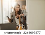 Shot of a multi-tasking young business woman looking on watch and using smartphone in her kitchen while getting ready to go to work.