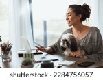 Small photo of Attractive young female freelancer working on laptop from her home and having her pet dog in her lap to keep her company.