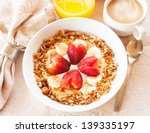 A healthy breakfast consisting of vanilla greek yogurt topped with granola, sliced bananas and strawberries shaped like hearts. Orange juice and coffee with steam are also present.