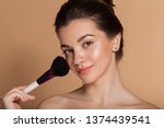 Closeup portrait of beautiful happy young girl with perfect skin is holding makeup brush in hand. Isolated on beige. Beauty and cosmetics concept.
