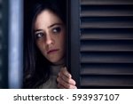 Worried Woman Watching Outside from a Wooden Window Shutter