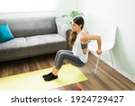 Small photo of Active and healthy young woman training at home. Beautiful woman in her 20s doing tricep dips with a chair in the living room