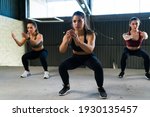 Small photo of Beautiful women doing a cardio HIIT routine and squatting. Three fit women in sportswear working out and doing squats in the gym