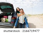 Portrait of an attractive young man piggybacking a woman while stopping at the side of road during a car trip