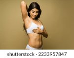 Small photo of Beautiful latin young woman in underwear raising her arm and doing a breast self examination to prevent cancer