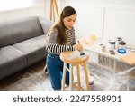 Small photo of Beautiful young woman painting a stool on her DIY home improvement project or furniture flipping