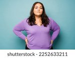 Small photo of Serious overweight hispanic woman with her hands on the hips looking determined while making eye contact