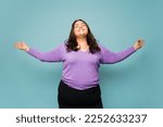 Relaxed happy overweight woman opening her arms looking carefree closing her eyes against a studio background