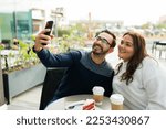 Cheerful influencer boyfriend and chubby girlfriend smiling taking a selfie with a smartphone while at the coffee shop to post it together on social media 