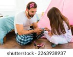 Beautiful little girl painting the nails of her happy loving father while having fun playing games in pajamas