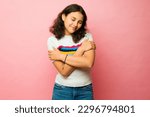 Small photo of Beautiful teen latin girl hugging herself and feeling self love and self esteem while looking relaxed in a pink studio background