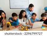 Latin male teacher helping his junior high students and teens to learn about coding and programming robot prototypes