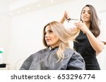 Pretty brunette working as a hairdresser and cutting hair tips of a female customer in a beauty salon