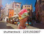 Woman hand hold  beautiful bright  sweet ice - cream cone with different flavors   held in hand on the background of  old street  in  Rovinj, Croatia