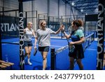 Small photo of Riga, Latvia - March 3, 2024 - Three women are on a padel court; two dressed in white are walking while the third in green and black gives a high-five, with sportsmanship on display.