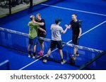Small photo of Riga, Latvia - March 3, 2024 - Players are engaged in a friendly exchange over the net on a padel court; two are shaking hands while another pair hugs, showing good sportsmanship.