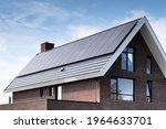 Solar panels mounted on the roof of a modern new-build house in a street in Heerenveen, Friesland, the Netherlands with sun and blue cloudy sky. Sustainable energy, electric power generation