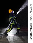 Small photo of Firefighter in fire fighting operation. Portrait of a heroic fireman in a protective suit and red helmet in action during heavy rain.