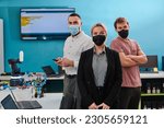 Small photo of A group of colleagues stand ingin a robotics laboratory, arms crossed, wearing protective masks, symbolizing their teamwork and commitment to technological innovation and scientific research.
