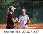 Small photo of Two female tennis players shaking hands with smiles on a sunny day, exuding sportsmanship and friendship after a competitive match.