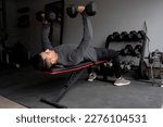 Young Man Bench Pressing Dumbbells at In Home Garage Gym