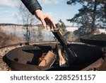 man reaching for a log on a campfire by a lake